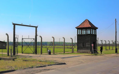 Auschwitz-Birkenau entrance gate and watchtower under clear sky.