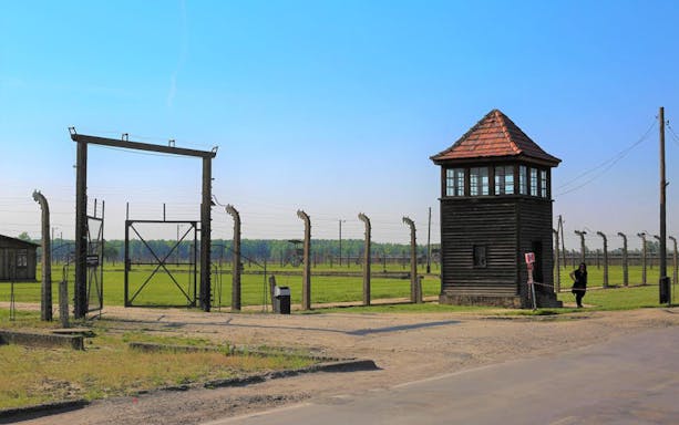 Auschwitz-Birkenau entrance gate and watchtower under clear sky.