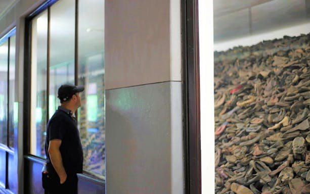 Visitor observing a display of shoes at Auschwitz-Birkenau Museum.