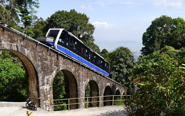Funicular train ascending Penang Hill with city view in background.