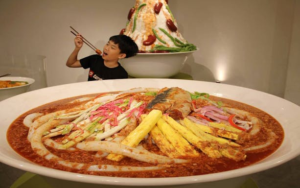 Giant bowl of Penang laksa at Wonderfood Museum, Georgetown, with a child using chopsticks.