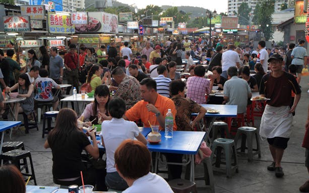 Crowded Penang Georgetown street food market with people dining at outdoor tables.