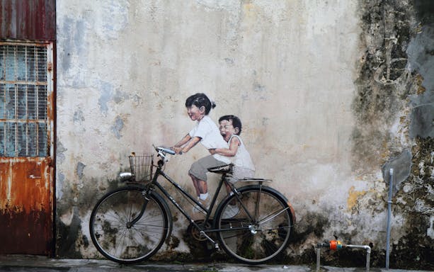 Street art of children on a bicycle in Georgetown, Penang, part of local food trail tour.