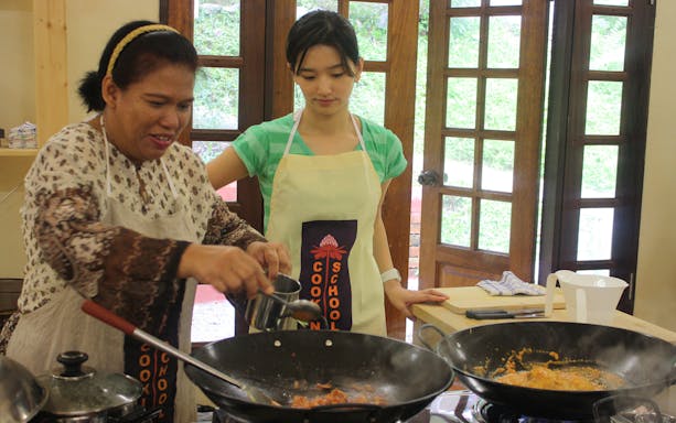 Cooking class in Penang with instructor and participant preparing a dish in a wok.