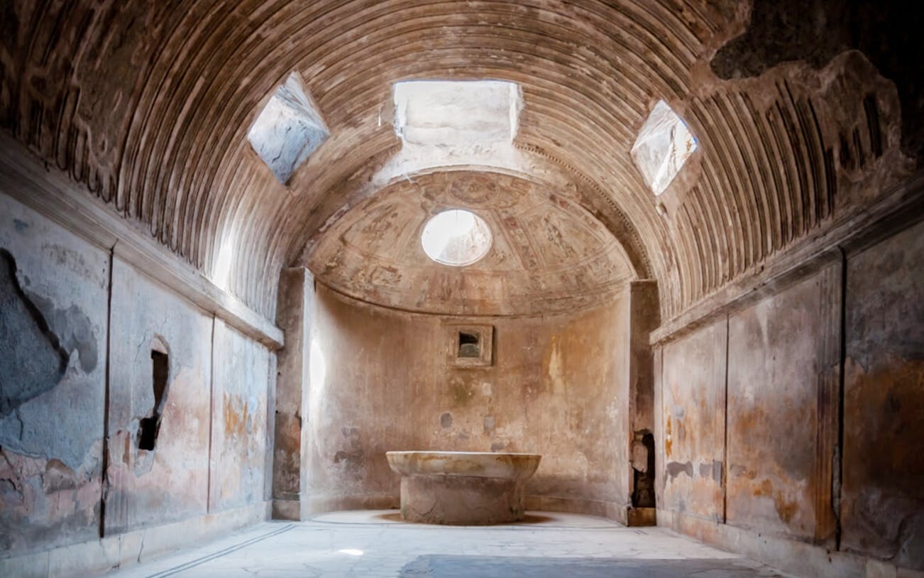 Ancient bathhouse interior in Pompeii, Italy, with arched ceiling and central basin.