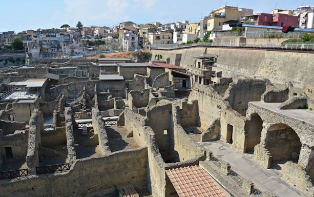 Ancient ruins of Pompeii with modern buildings in the background, part of Naples tour.