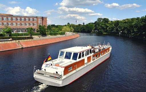 Boat cruising on the Spree River in Berlin with cityscape and TV tower in the background.