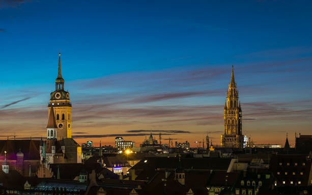 Munich skyline at sunset featuring St. Peter's Church and New Town Hall towers.