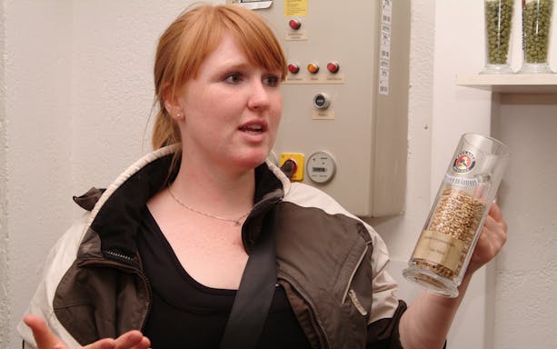 Tour guide explaining beer brewing process with malt grains in a glass.