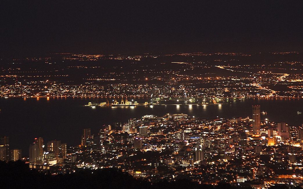 Night view of Penang cityscape from Penang Hill, Malaysia, with illuminated buildings and coastline.