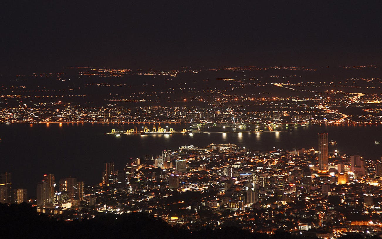 Night view of Penang cityscape from Penang Hill, Malaysia, with illuminated buildings and coastline.