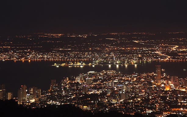 Night view of Penang cityscape from Penang Hill, Malaysia, with illuminated buildings and coastline.