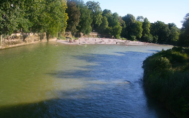 Riverbank in English Garden, Munich, with people relaxing on the beach.