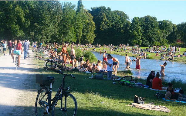 Cyclists and people relaxing by the river in the English Garden, Munich.