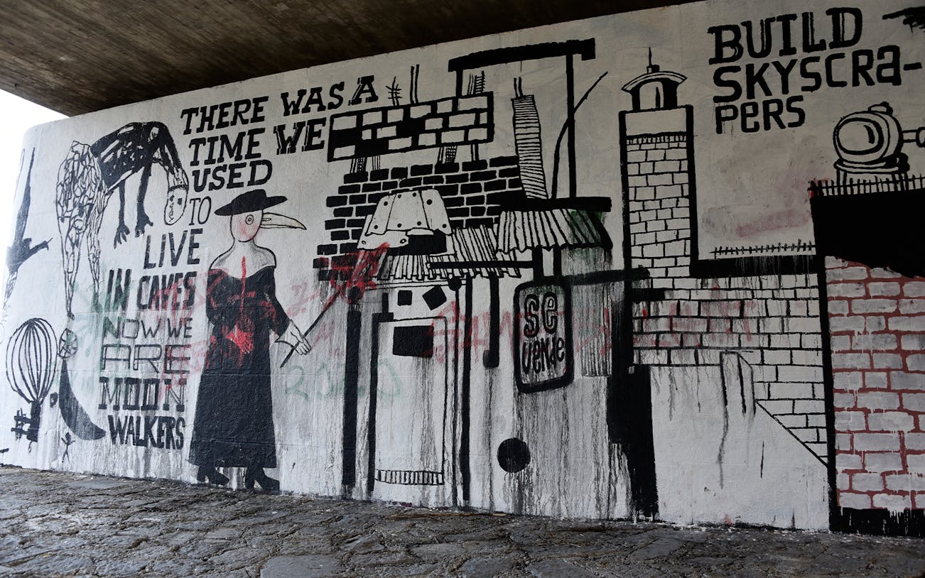 Street art mural with abstract figures and text under a bridge in Munich.