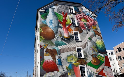 Street art mural on a Munich building featuring surreal objects and vibrant colors.