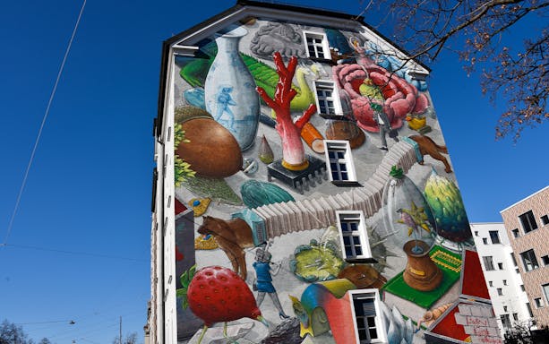 Street art mural on a Munich building featuring surreal objects and vibrant colors.