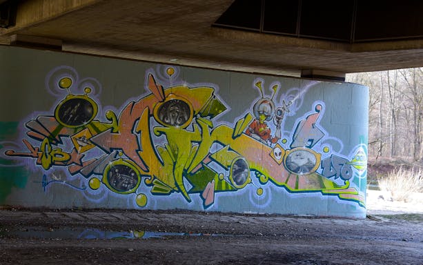 Street art mural featuring colorful abstract shapes and alien figures under a bridge in Munich.