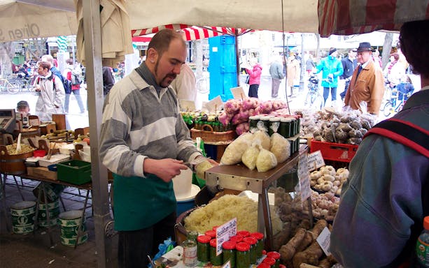 Vendor preparing sauerkraut at a Bavarian market stall with various local produce.