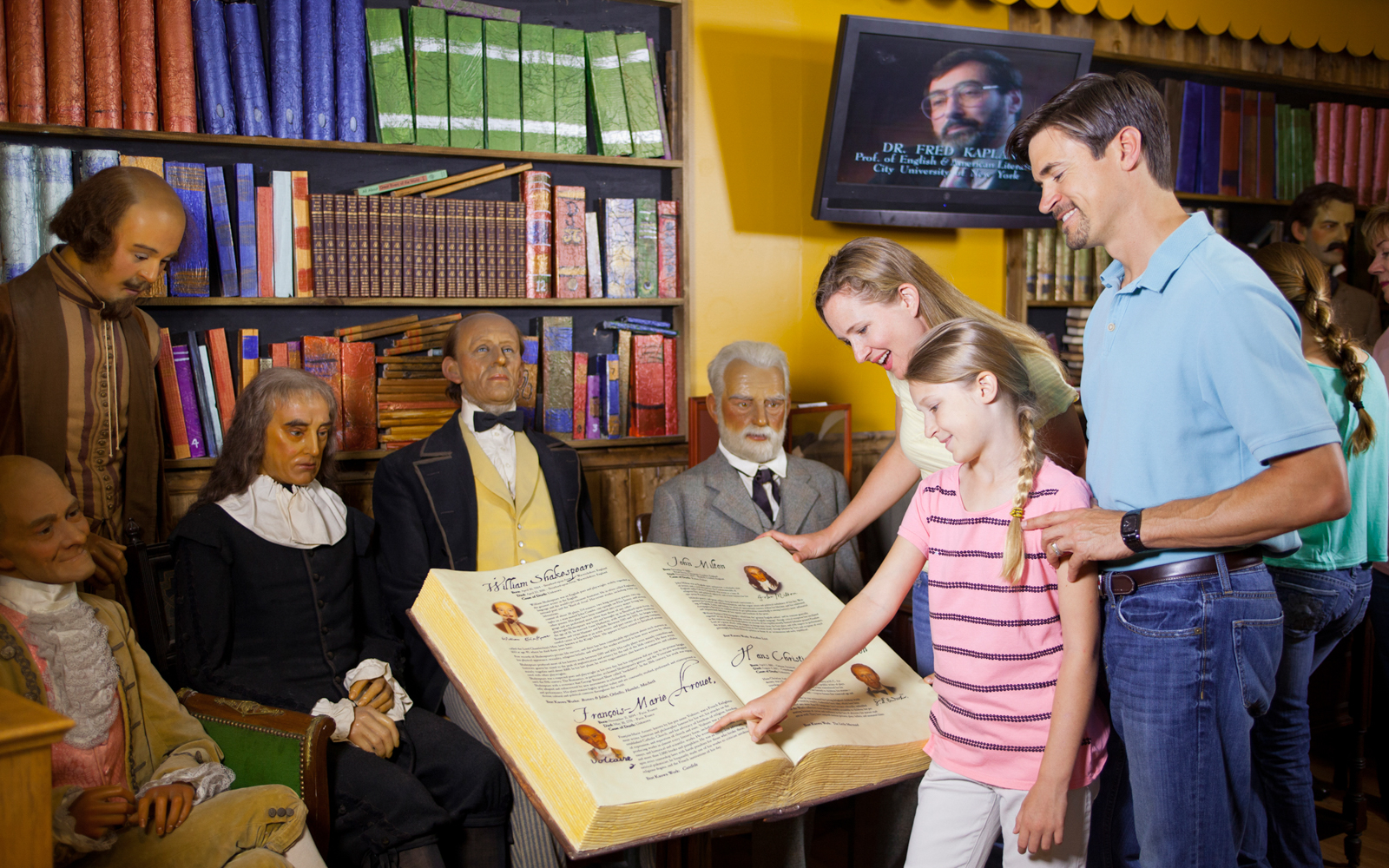 Family exploring wax figures and historical book at St. Augustine Potter's Wax Museum.