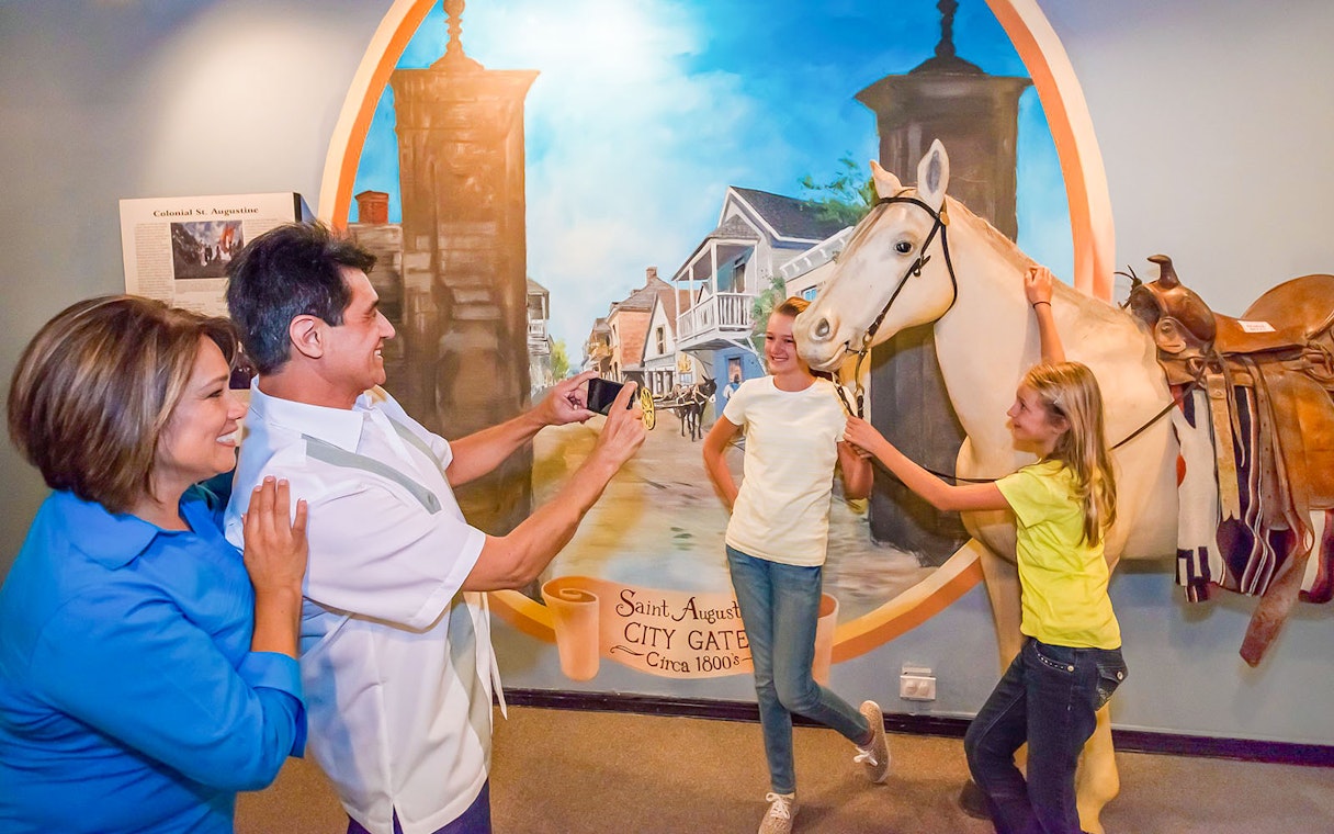 Family enjoying St. Augustine History Museum exhibit with city gate mural and horse display.