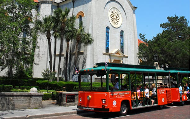 St. Augustine Old Town Trolley in front of historic church with palm trees.