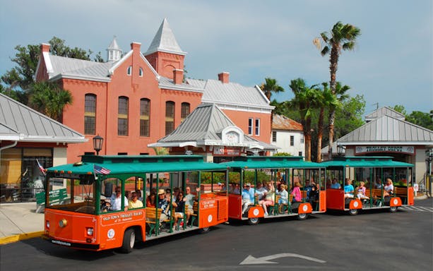 St. Augustine Old Town Trolley with tourists in front of historic red brick building.