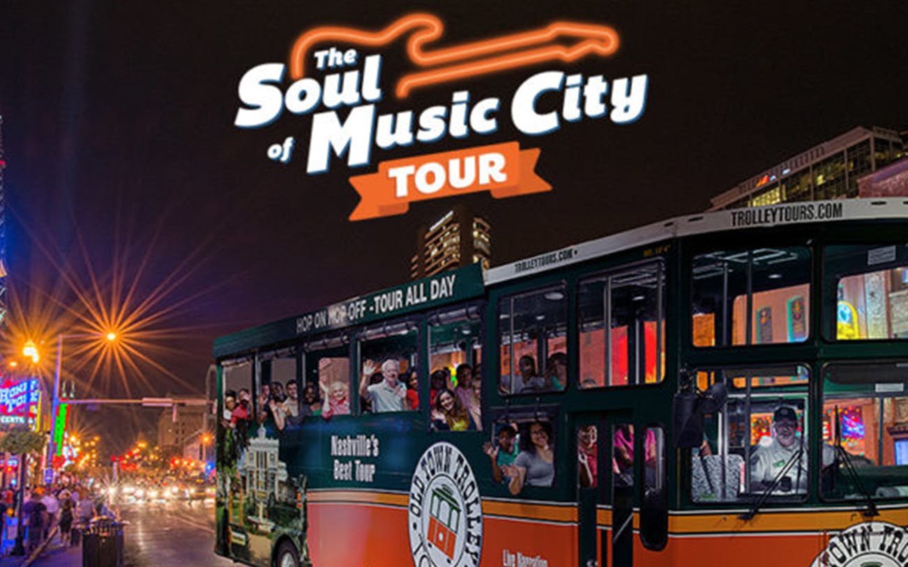 Nashville night tour bus with passengers on a city street, neon lights in the background.