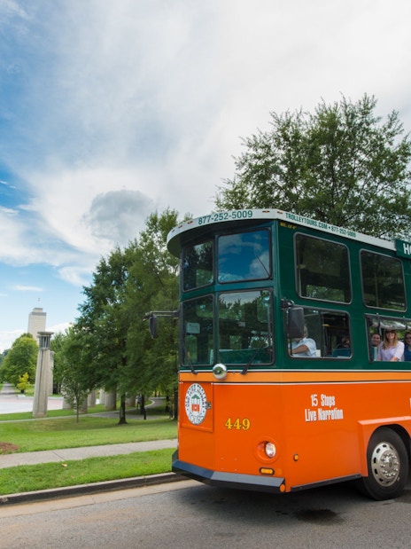 Nashville hop-on hop-off trolley with tourists, city skyline in background.