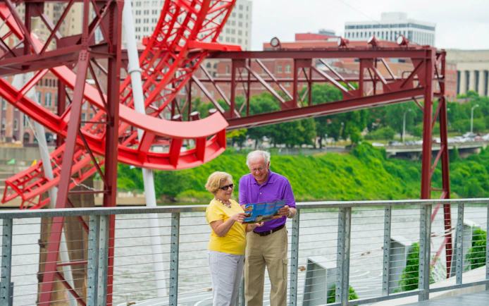 Elderly couple reading a map near a red sculpture on a Nashville riverfront walkway.