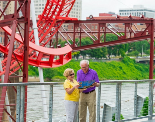 Elderly couple reading a map near a red sculpture on a Nashville riverfront walkway.