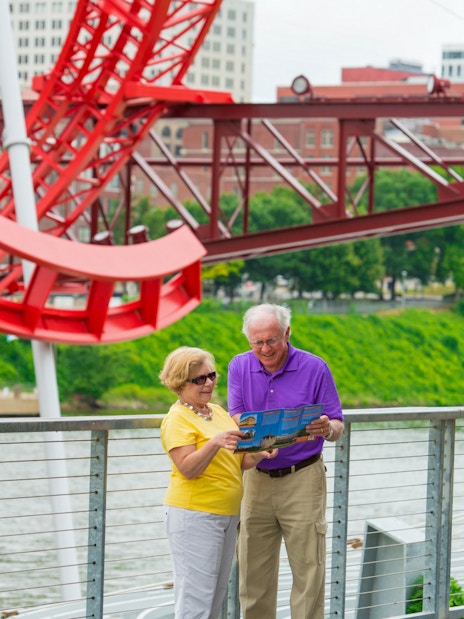 Elderly couple reading a map near a red sculpture on a Nashville riverfront walkway.