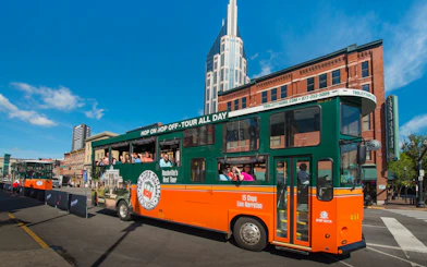 Nashville Old Town Trolley with tourists on a city street, featuring a tall building in the background.