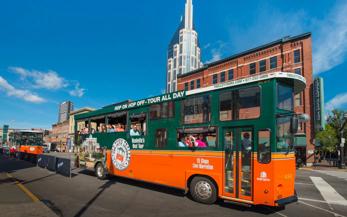 Nashville Old Town Trolley with tourists on a city street, featuring a tall building in the background.