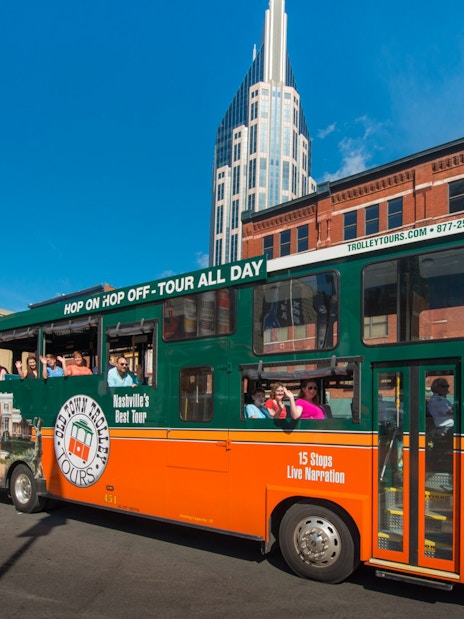 Nashville Old Town Trolley with tourists on a city street, featuring a tall building in the background.