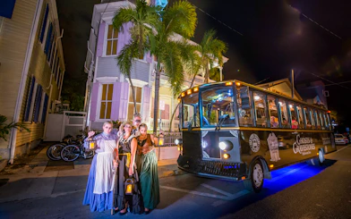 Tour group in historical costumes with lanterns beside Boston Ghosts & Gravestones trolley at night.