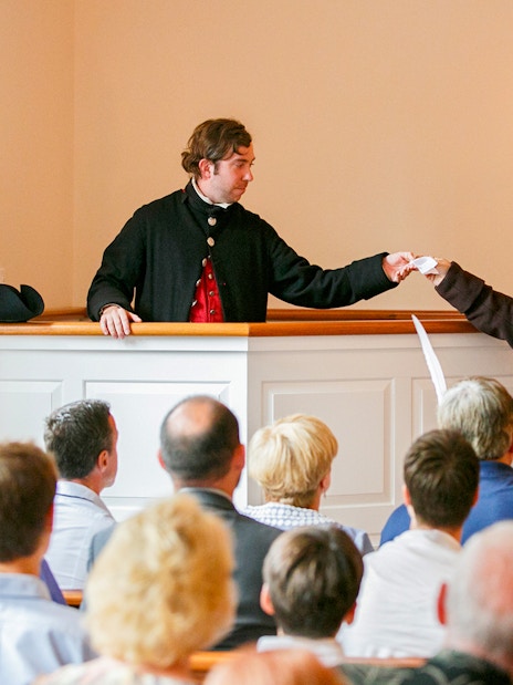 Reenactment of Boston Tea Party debate with actors in period costumes inside a historic room.