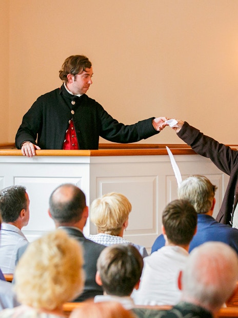Reenactment of Boston Tea Party debate with actors in period costumes inside a historic room.