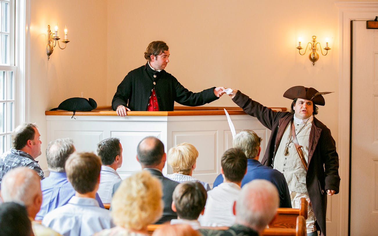 Reenactment of Boston Tea Party debate with actors in period costumes inside a historic room.