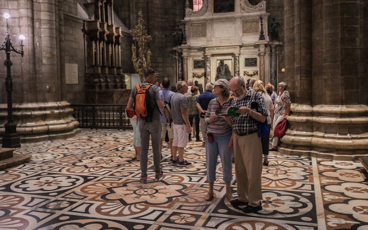 Tourists exploring the interior of Milan Duomo with intricate floor designs.