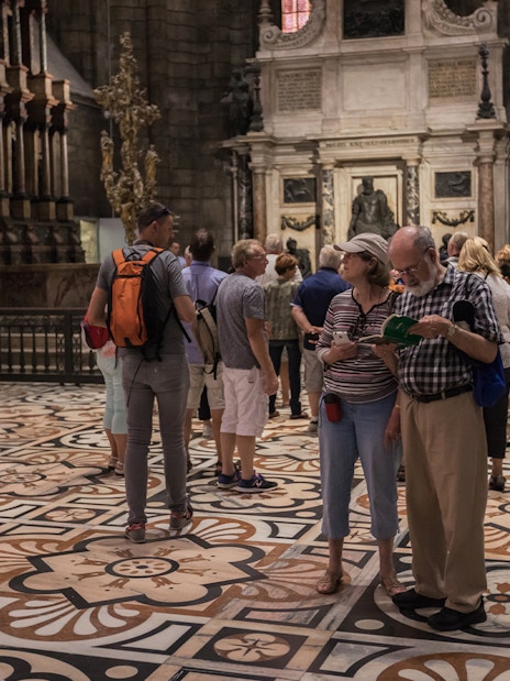 Tourists exploring the interior of Milan Duomo with intricate floor designs.