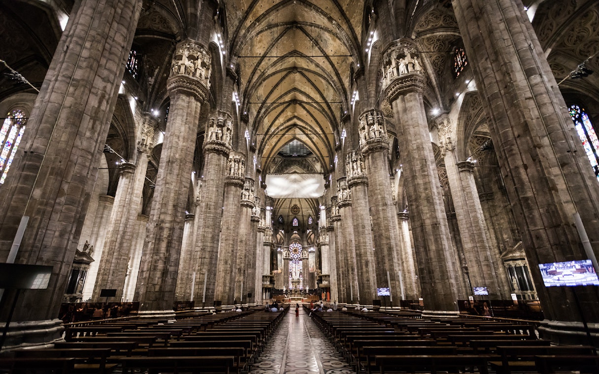 Interior view of Milan Duomo with towering columns and ornate ceiling.