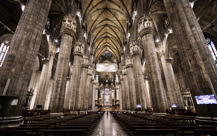 Interior view of Milan Duomo with towering columns and ornate ceiling.