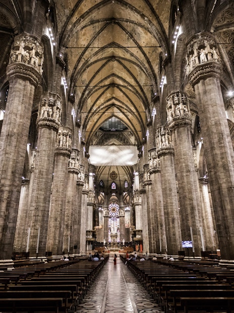 Interior view of Milan Duomo with towering columns and ornate ceiling.