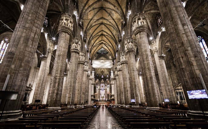 Interior view of Milan Duomo with towering columns and ornate ceiling.