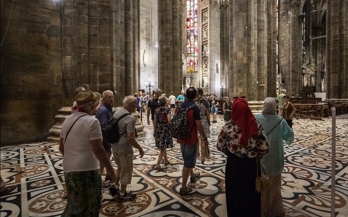Tourists inside Duomo di Milano admiring stained glass windows and architecture.