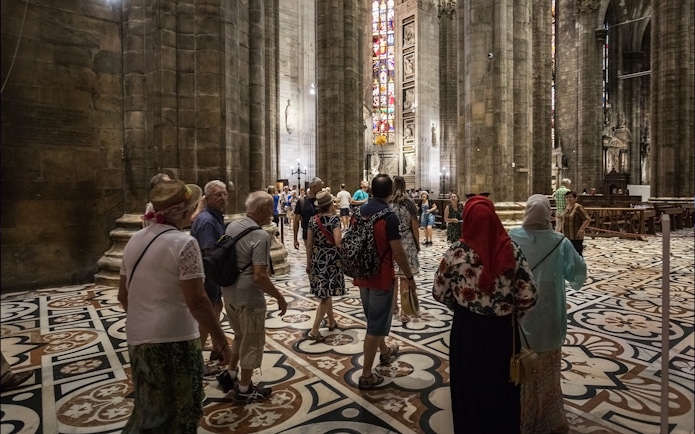 Tourists inside Duomo di Milano admiring stained glass windows and architecture.
