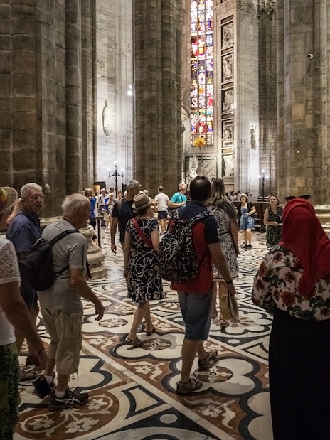 Tourists inside Duomo di Milano admiring stained glass windows and architecture.