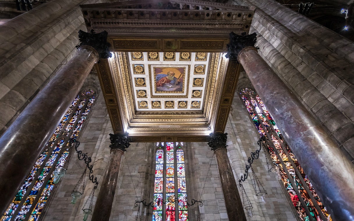 Interior view of Milan Duomo ceiling with stained glass windows and ornate columns.