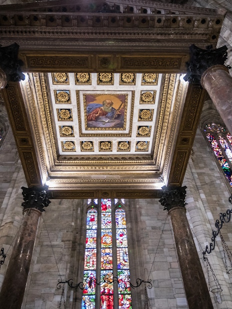 Interior view of Milan Duomo ceiling with stained glass windows and ornate columns.